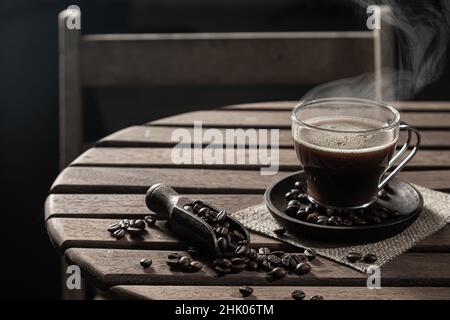 Hot coffee in a glass cup and  coffee beans on wooden table on dark background. Stock Photo