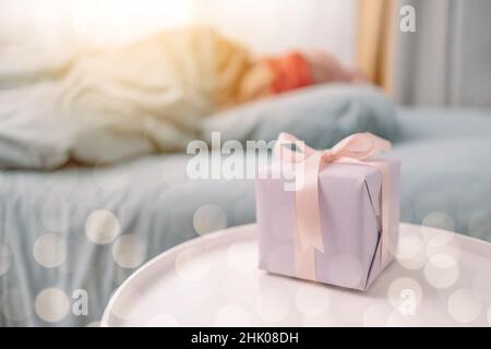 Woman in red sleep mask sleeping in bed near paper gift box with pink satin ribbon decor. Christmas, New Year, Valentine's Day and birthday concept Stock Photo