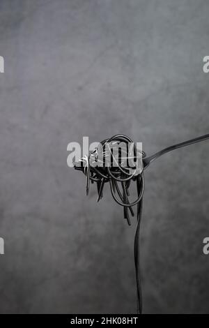 Hot black pasta rolled on a fork on gray background with copyspace. Vertical format. Stock Photo