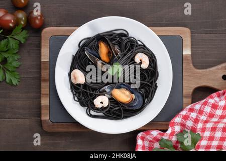 Plate of black pasta with seafood on wooden background. Top view. Stock Photo
