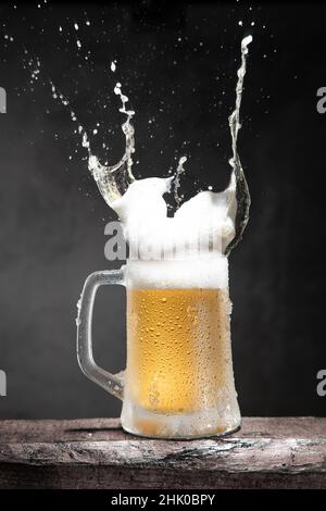 Mug of beer with foam and splashes on wooden table isolated on dark background. Vertical format. Stock Photo