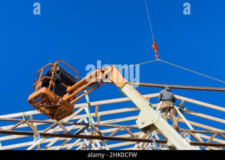 Aerial view of a professional builder nailing wood beams on the roof of unfinished wooden frame house in using air hammer Stock Photo