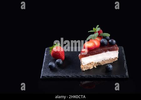 Piece of cheesecake with fresh strawberries and blueberries isolated  served on slate plate on black background with copyspace. Homemade bakery concep Stock Photo