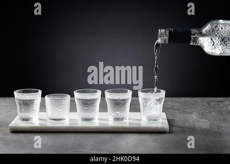 Pouring cold vodka into shot glass isolated on dark background. Selective focus. Stock Photo