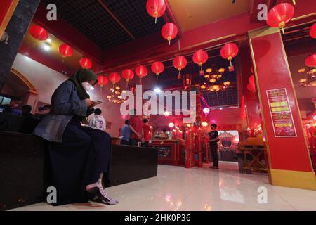 Bekasi, Wast Java, Indonesia. 31st Jan, 2022. A Muslim woman wearing a hijab is seen using a cellphone while the congregation is praying on the eve of the Chinese New Year at the Hok Lay Kiong Temple, which was founded in the 18th century and is the first and largest pagoda in the city of Bekasi, West Java, Indonesia, on January 31, 2022. Because it is still in the atmosphere of the Covid-19 pandemic and in the midst of increasing Covid-19 cases, the Omricon variant, by the temple management, tonight's worship is held in a limited manner and the number of people allowed to pray is a maximum Stock Photo