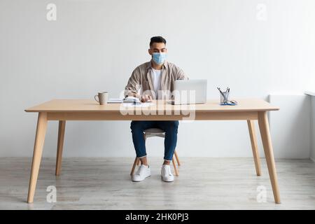 Man in protective facemask working on pc at home office Stock Photo
