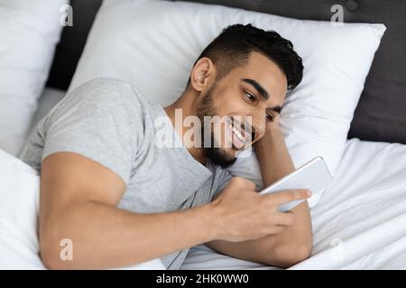 Closeup Shot Of Handsome Arab Man Resting In Bed With Smartphone Stock Photo