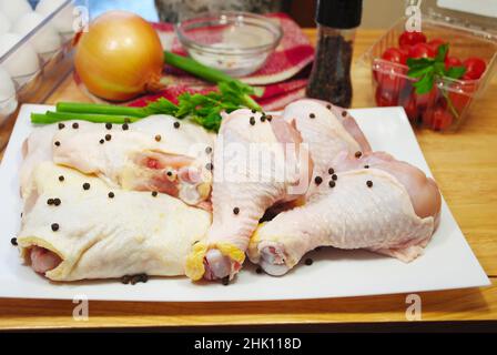 Raw Chicken Legs and Thighs on a Plate with Fresh Black Peppercorns Stock Photo
