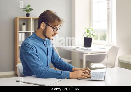 Portrait of young serious man working hard on laptop in bright modern coworking center. Stock Photo