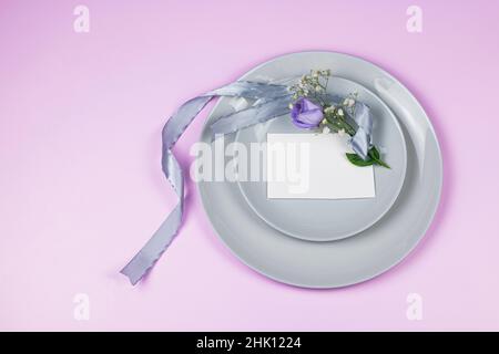 Holiday greeting mockup scene. Blank greeting cards, grey plates, and violet flowers eustoma with ribbon on pink background with copy space. Flat lay, Stock Photo