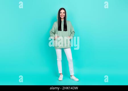 Full size photo of sweet millennial brunette lady stand wear sweatshirt pants sneakers isolated on teal background Stock Photo