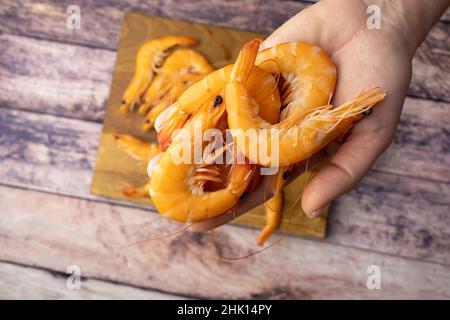 boiled shrimp, unpeeled, holds in his hands against the background of a wooden table Stock Photo