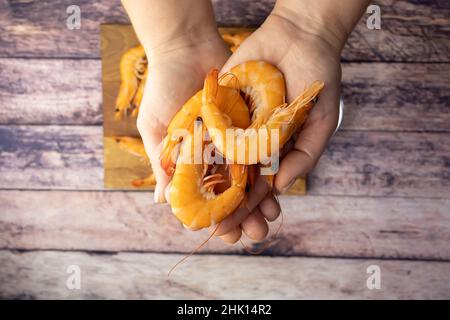 boiled shrimp, unpeeled, holds in his hands against the background of a wooden table Stock Photo
