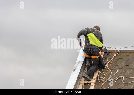 A man works on the roof repair, installs sheet metal on top of the gable wall Stock Photo