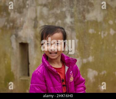 Vietnamese little girl with sincerely smile. Purple clothes of a girl on the background of an old yellow wall, a great combination Stock Photo