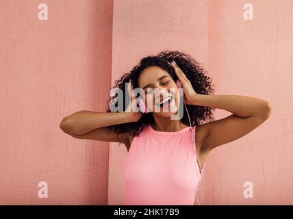 Portrait of a young laughing woman wearing pink headphones standing with closed eyes Stock Photo