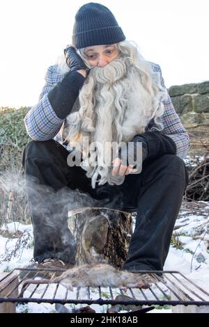 The homeless man grills a rat in the snowy outskirts of the city. Stock Photo