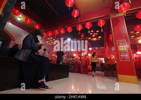 Bekasi, Wast Java, Indonesia. 31st Jan, 2022. A Muslim woman wearing a hijab is seen using a cellphone while the congregation is praying on the eve of the Chinese New Year at the Hok Lay Kiong Temple, which was founded in the 18th century and is the first and largest pagoda in the city of Bekasi, West Java, Indonesia, on January 31, 2022. Because it is still in the atmosphere of the Covid-19 pandemic and in the midst of increasing Covid-19 cases, the Omricon variant, by the temple management, tonight's worship is held in a limited manner and the number of people allowed to pray is a maximum Stock Photo