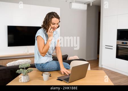 Busy woman talking with a customers on the phone and types on the keyboard, while sitting at the office desk. Multitasking female office employee concept Stock Photo