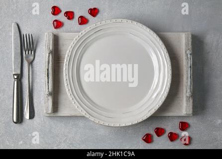 White plate with cutlery on a light wooden tray surrounded by red hearts Stock Photo