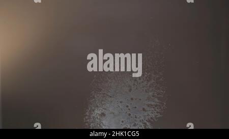 Close up of sprayed alcohol containing liquid on glass transparent surface. Bottom view of the liquid stain foaming on glass table. Stock Photo