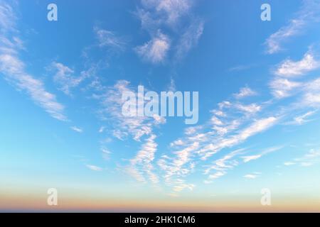Rarefied cirrus cloud stripes high in a bright blue sky. Beautiful azure skyscape at evening. Sparse white clouds over the horizon. Tranquil heaven. Stock Photo