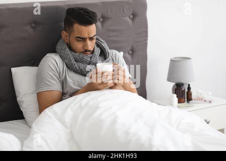 Cold And Flu. Portrait Of Sick Arab Man Drinking Tea In Bed Stock Photo