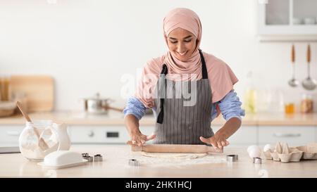 Portrait Of Cheerful Islamic Housewife Wearing Hijab And Apron Baking In Kitchen Stock Photo