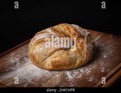 A freshly made loaf of sourdough bread dusted in flour on a board with a black background. Stock Photo