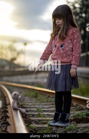 girl scolds her teddy bear on a train track Stock Photo