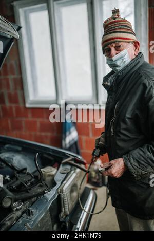 Old man with protective mask in the garage looking at camera. Stock Photo