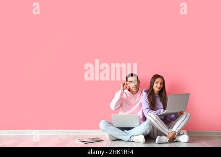 Young couple with laptops sitting near pink wall Stock Photo