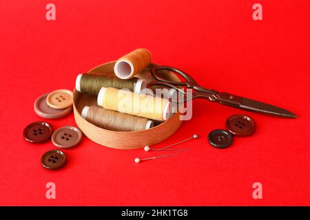 Wooden lid with sewing thread spools, scissors and buttons on color background Stock Photo