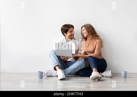Smiling millennial european man and woman sitting on floor resting from moving at new house, planning interior Stock Photo