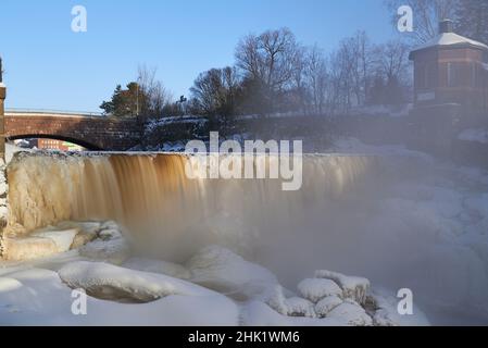 Helsinki, Finland - February 18, 2021: Water pours over frozen museum dam in the mouth of Vantaa River at the Vanhankaupunginkoski rapids (Vanhankaupu Stock Photo