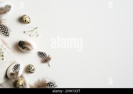 Elegant Easter flatlay composition. Stylish Easter eggs decorated feathers with gypsophila flowers on white table. Flat lay, top view, copy space. Stock Photo