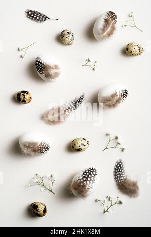 Happy Easter flat lay composition. Easter eggs decorated feathers with gypsophila flowers on white background. Elegant, minimal style. Stock Photo