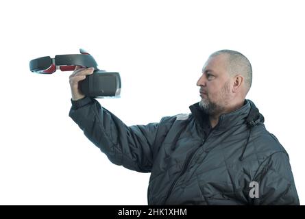 A man holds vr glasses in his hand in front of him and looks at them. Stock Photo