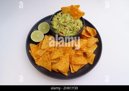 Guacamole sauce and tortilla chips or nachos in black plate isolated on a white background Stock Photo