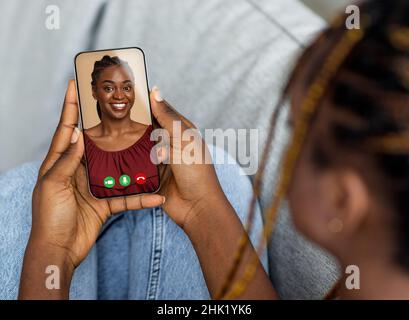 Remote communication concept. Young black lady using cellphone to talk to her friend online from home Stock Photo