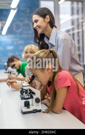 Girl looking through microscope and teacher with boys Stock Photo