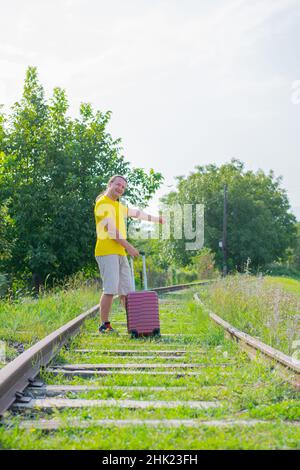 a cheerful man with a suitcase is walking on the railroad Stock Photo