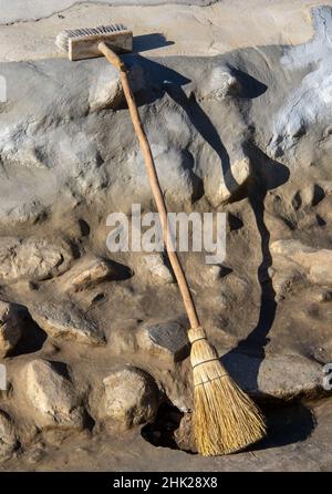 A broom made from grass and a large paint brush isolated next to a stone wall Stock Photo