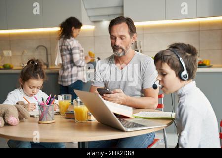 Father using smartphone while his kids doing homework Stock Photo