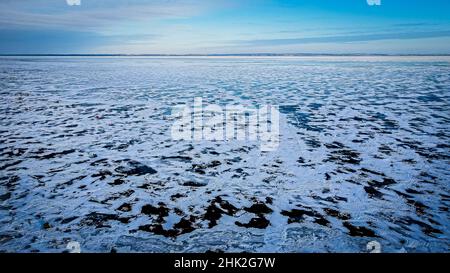 Snow partially covers the frozen lake surface. Scenic sky above with a frozen surface. The other side of the lake can be seen. Stock Photo