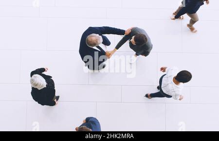 Lets look at the bigger picture. Cropped shot of two unrecognizable businesspeople shaking hands while in the office with their colleagues during the Stock Photo