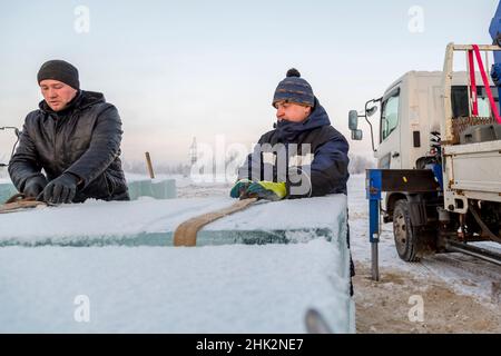 Workers in winter suits wind slings under an ice block at a construction site Stock Photo