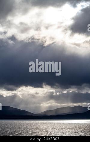 Chile, Patagonia. Rays of sunlight breaking through clouds over the sea and mountains. Stock Photo
