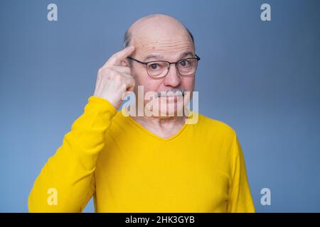 Senior man in glasses holding fingers on his temple, trying to remember thing or word. Stock Photo