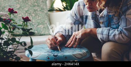 Close up of woman at work paiting with blue and mandala concept an old footstool at home sitting outside. Female people in hobby leisure activity with Stock Photo